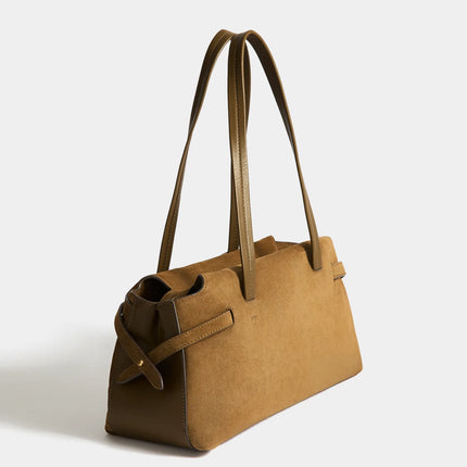 A tan suede handbag with dual shoulder straps and a small gold-tone metal logo plaque on the front, photographed against a clean white background.