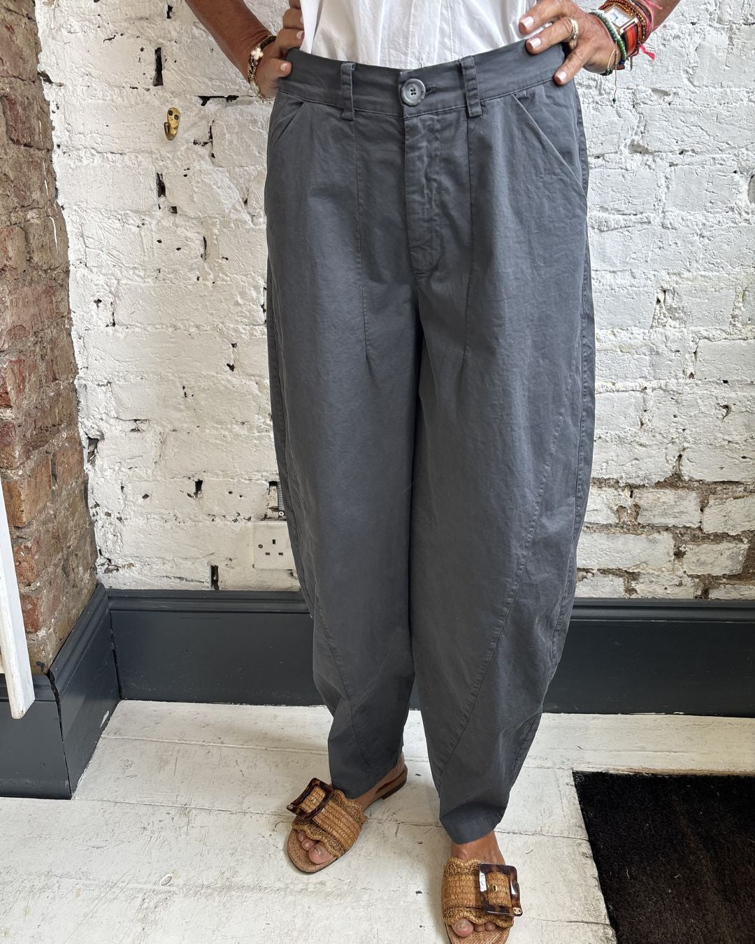 Person wearing gray pants standing in a room with a white brick wall.