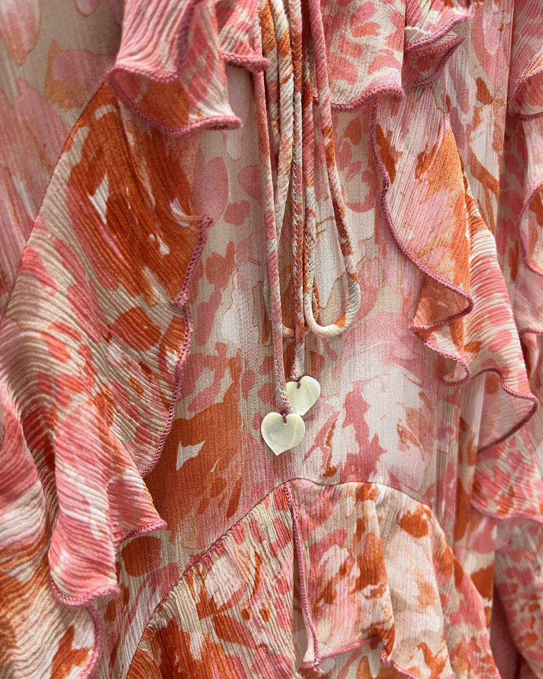 Close-up of a floral patterned garment with ruffled edges and a necklace.