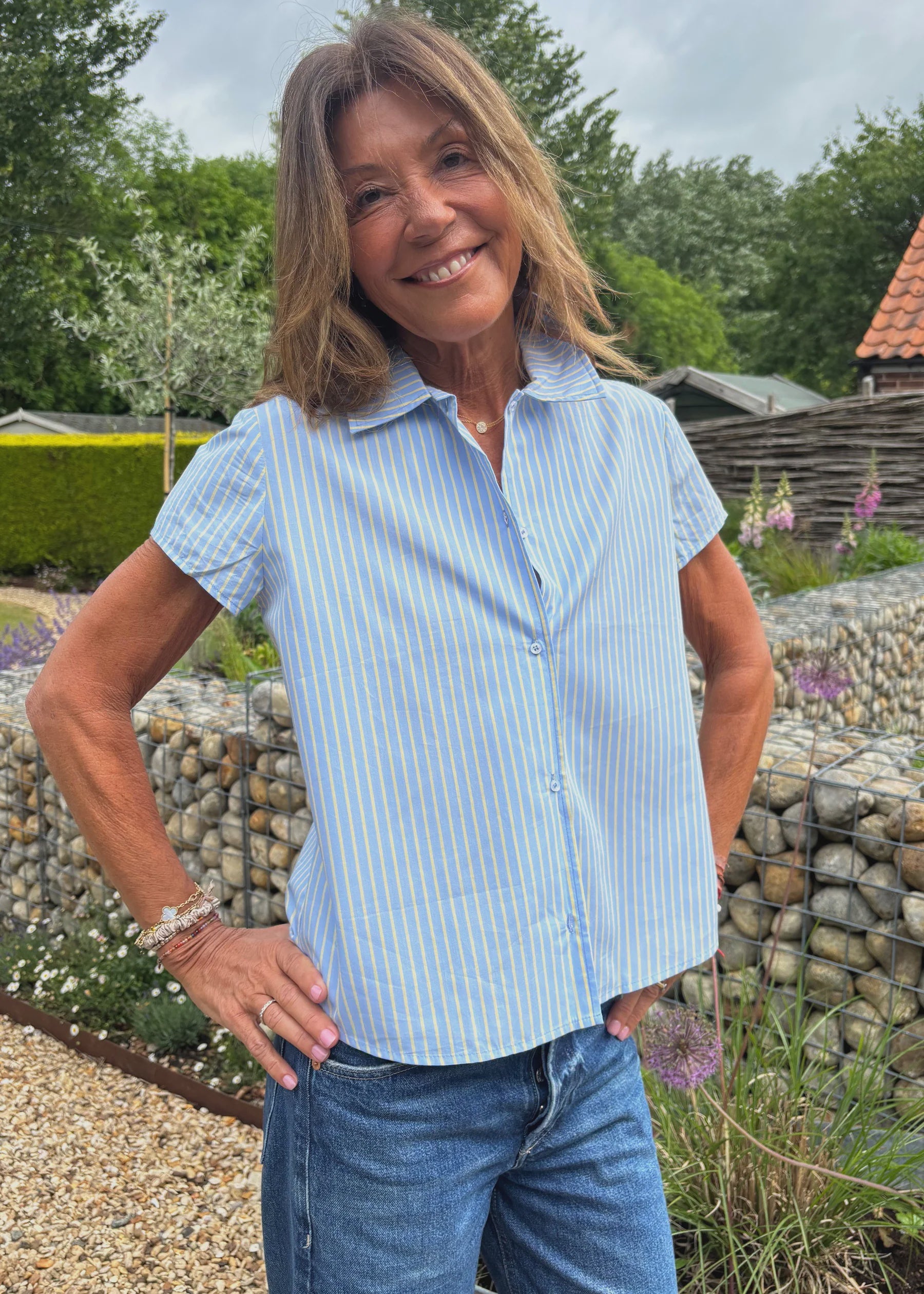 Woman wearing a light blue striped shirt and jeans standing in a garden.