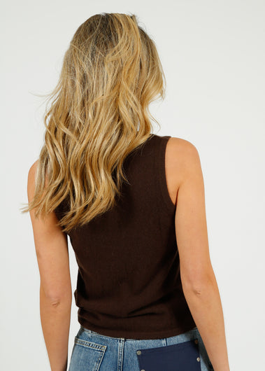 Woman wearing a brown sleeveless top and blue jeans with sunglasses on a white background