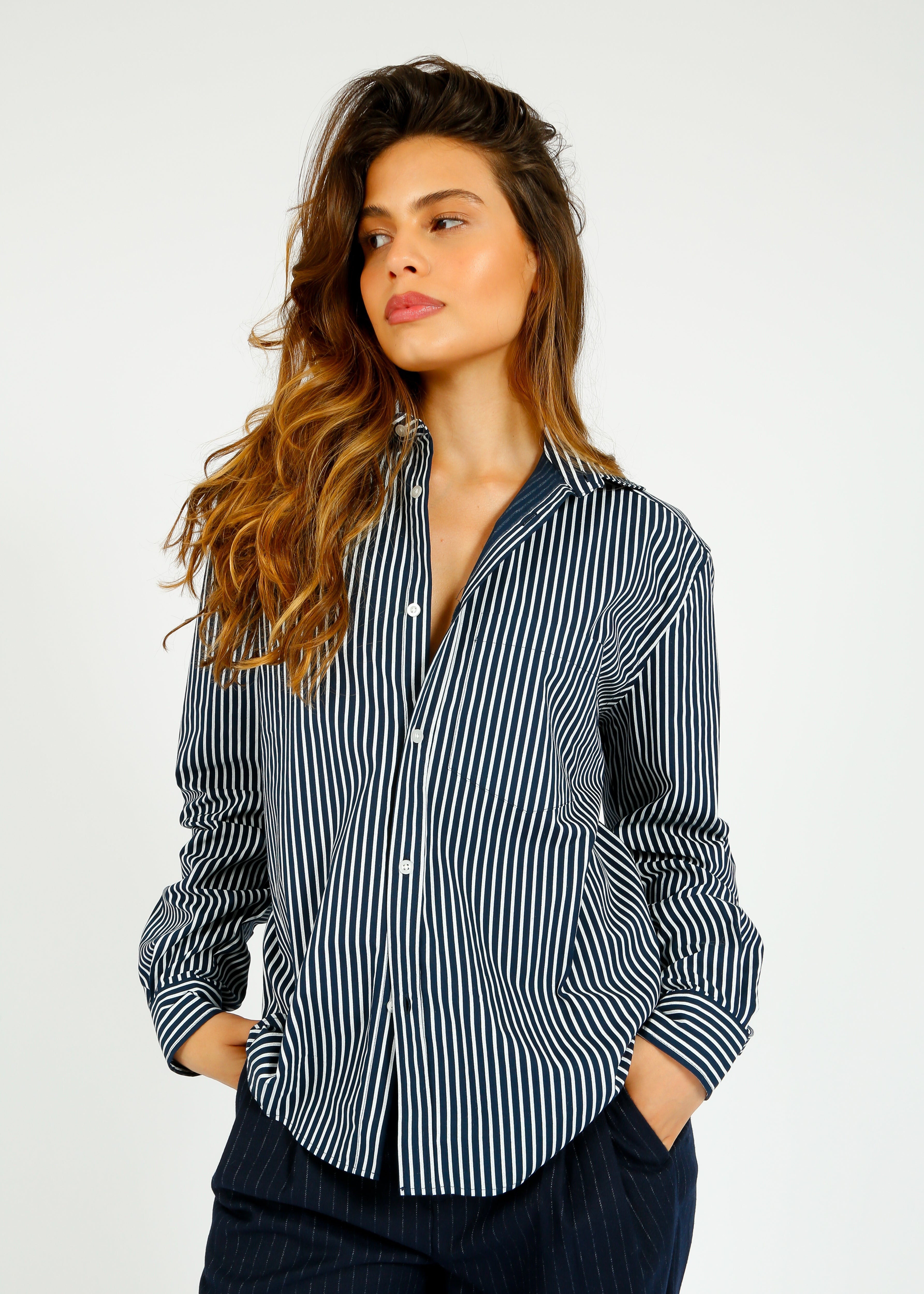 A woman wearing a navy and white striped, classic fit, button-down shirt with a collar and a breast pocket.