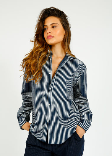 A woman wearing a navy and white striped, classic fit, button-down shirt with a collar and a breast pocket.