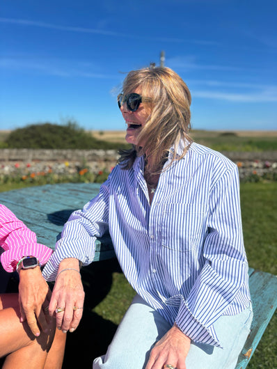 An older person sitting outdoors wearing a blue and white striped button-down shirt with a classic collar.