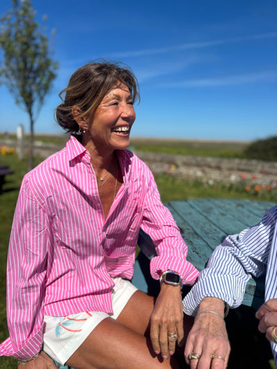A person wearing a pink and white striped button-down shirt with a classic collar, sitting outdoors.
