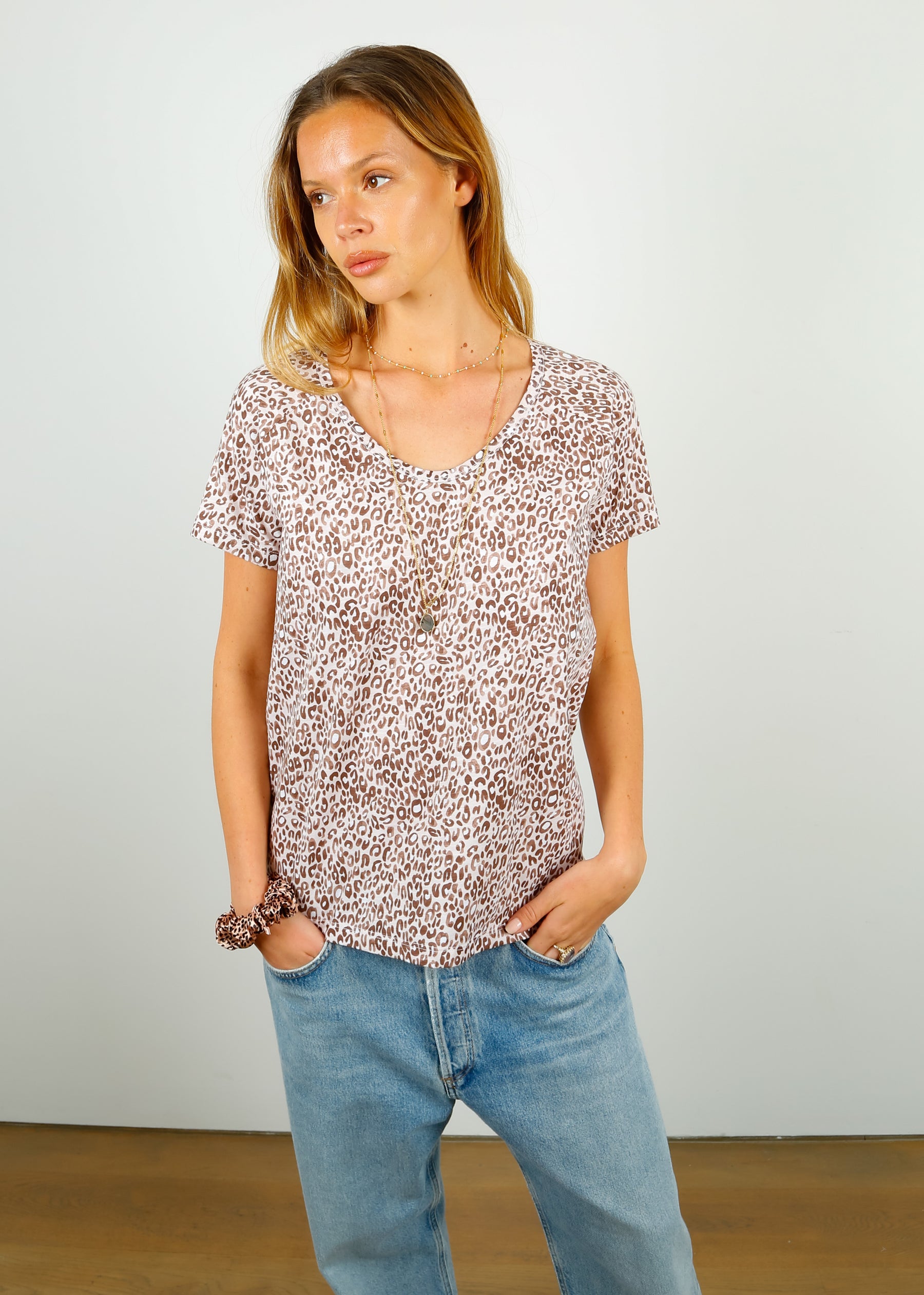 A woman wearing a leopard print cotton V-neck t-shirt in beige and light brown colors, paired with blue jeans.