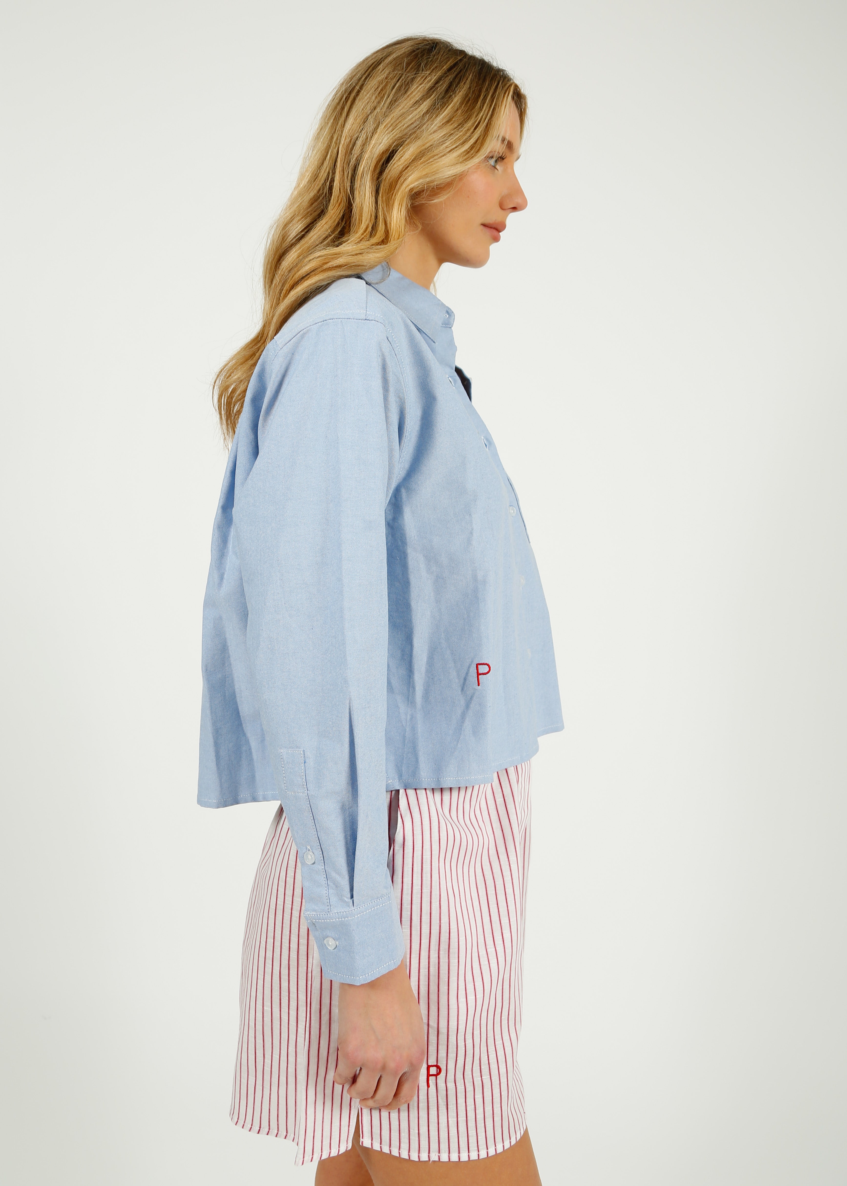 PARK Holkham Shirt in Oxford Blue Woman wearing a light blue shirt over a striped dress on a white background
