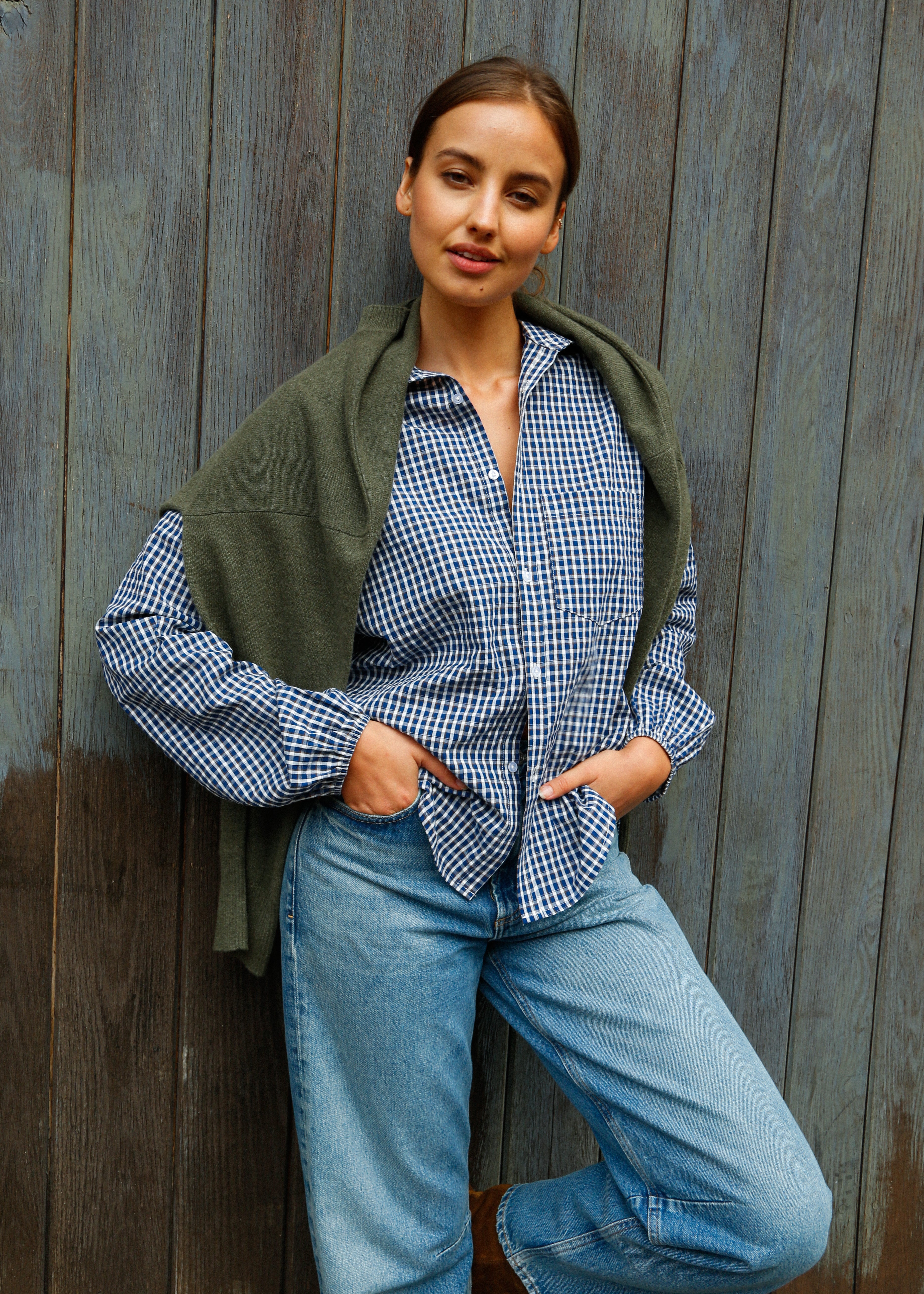 Woman wearing a green shawl over a checkered shirt and blue jeans against a wooden background