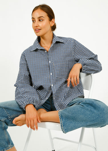 Woman wearing a green shawl over a checkered shirt and blue jeans against a wooden background