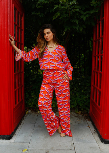 A person standing in front of a red telephone box wearing orange wide-leg trousers with a ribbon print.