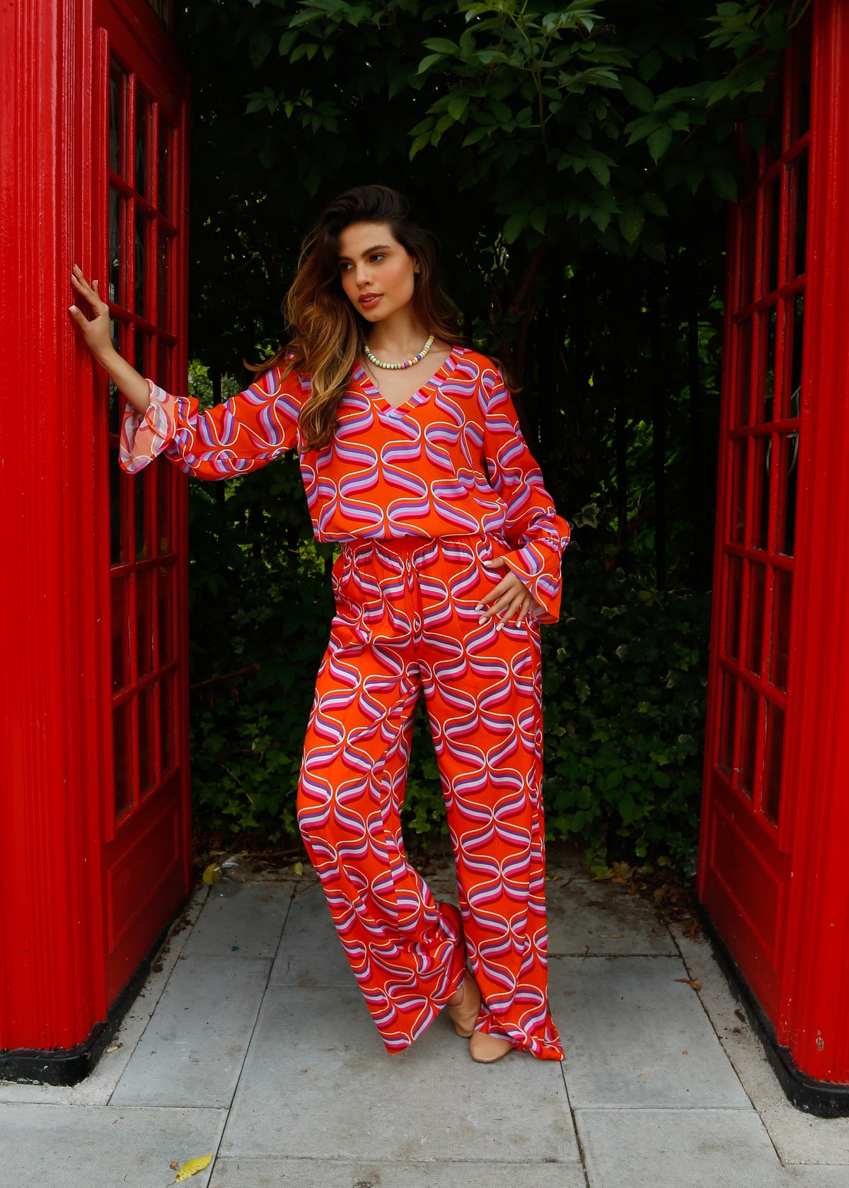A person standing in front of a red telephone box wearing orange wide-leg trousers with a ribbon print.