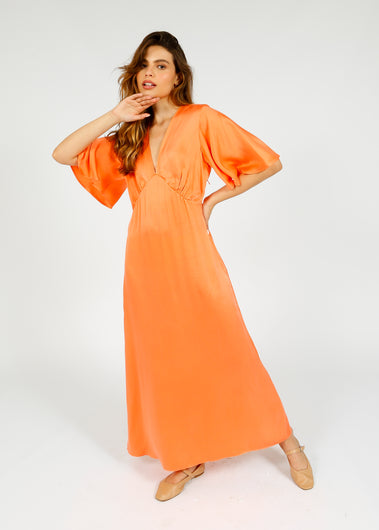 A woman modeling a salmon-colored, maxi-length silk dress with a V-neck bodice and flutter sleeves.