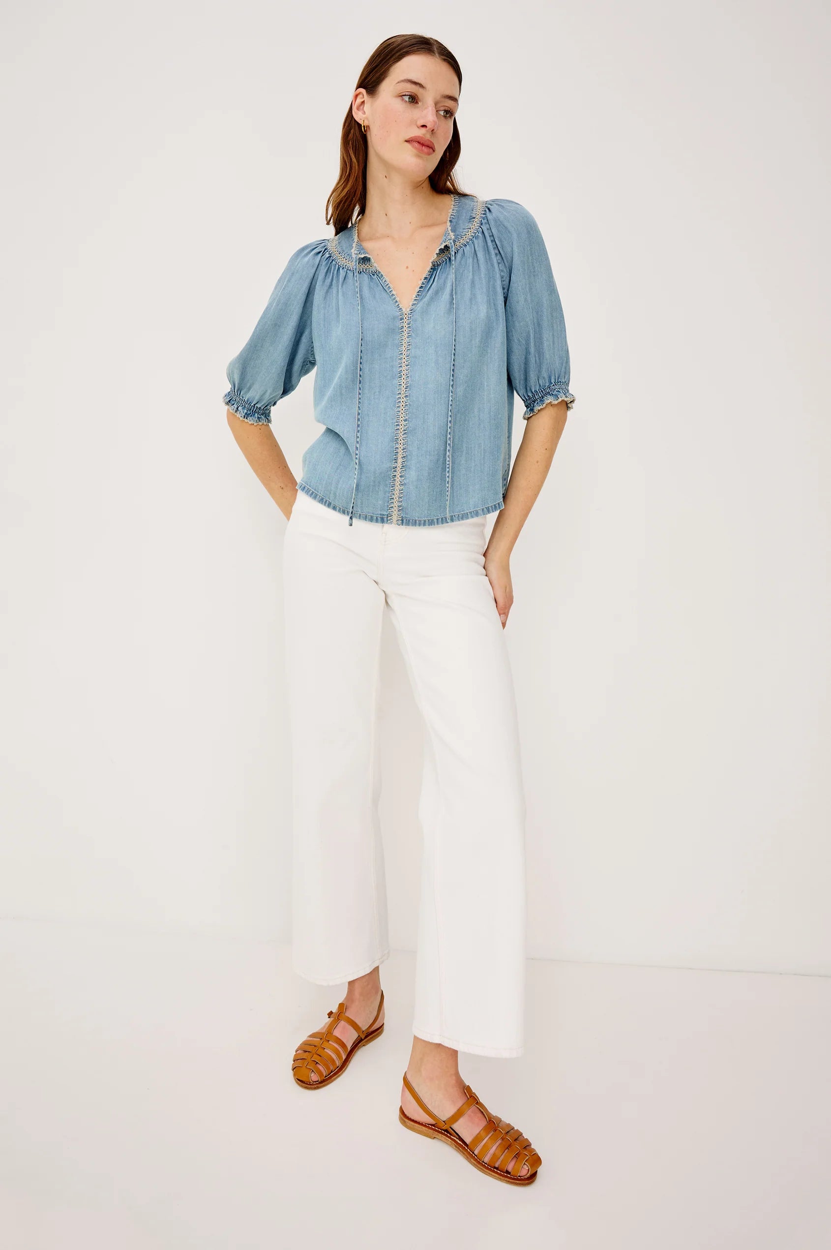 Woman wearing a blue denim shirt, white pants, and brown sandals on a white background