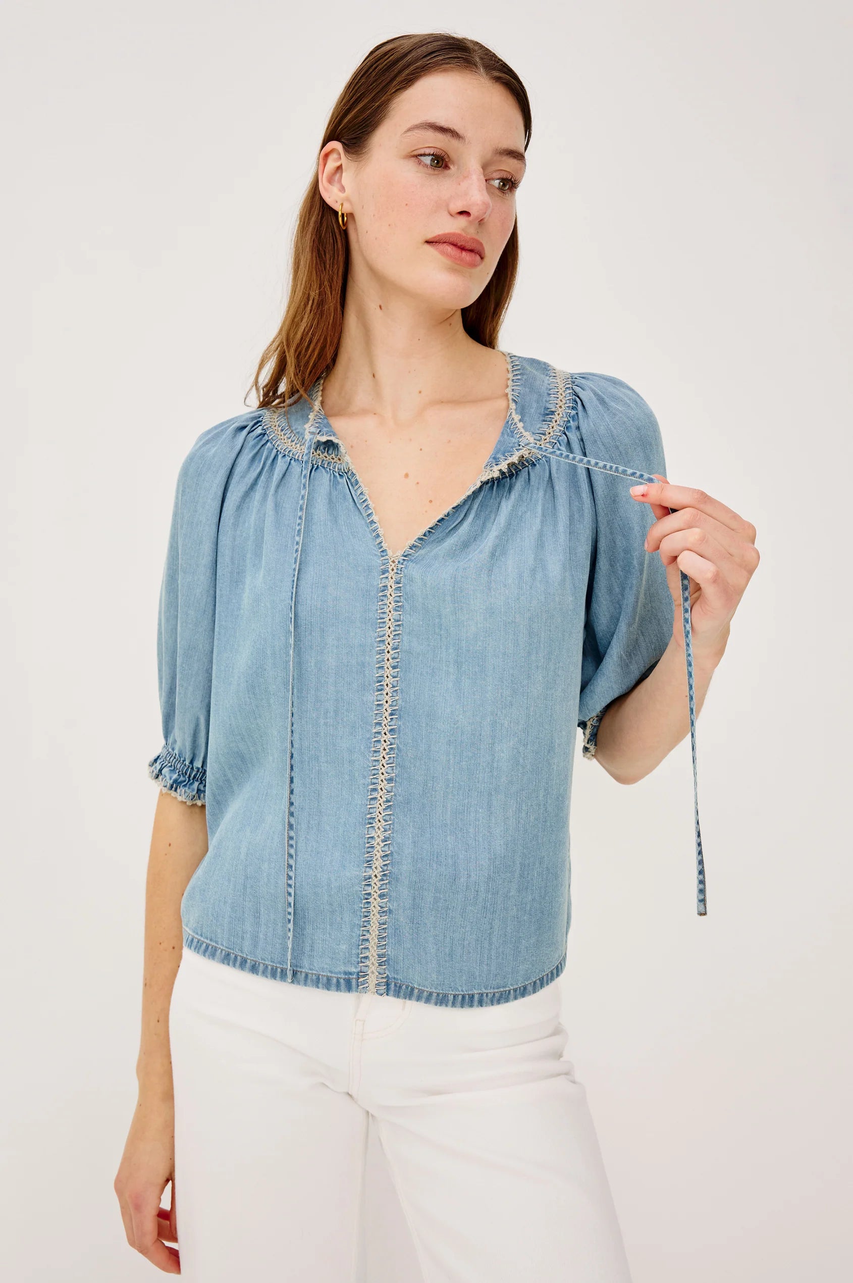 Woman wearing a light blue denim blouse with white pants on a plain background