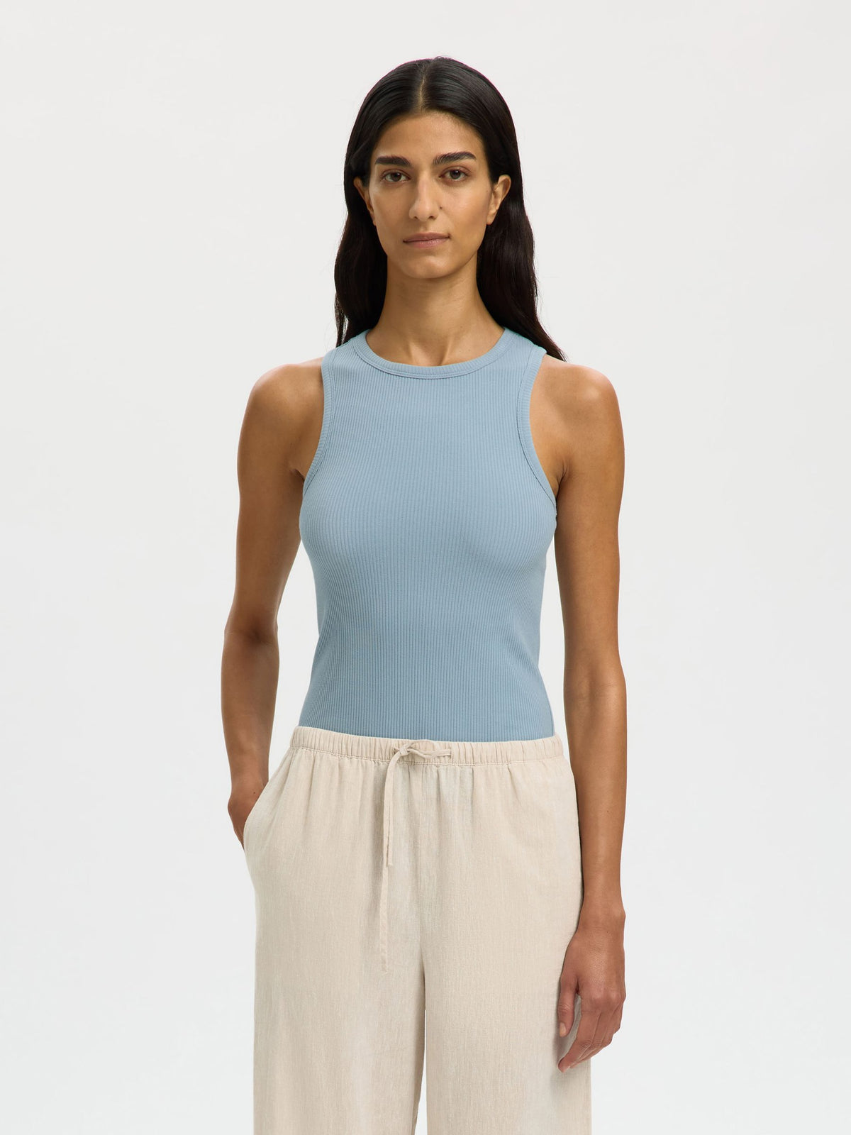 Woman wearing a light blue sleeveless top and beige pants on a white background