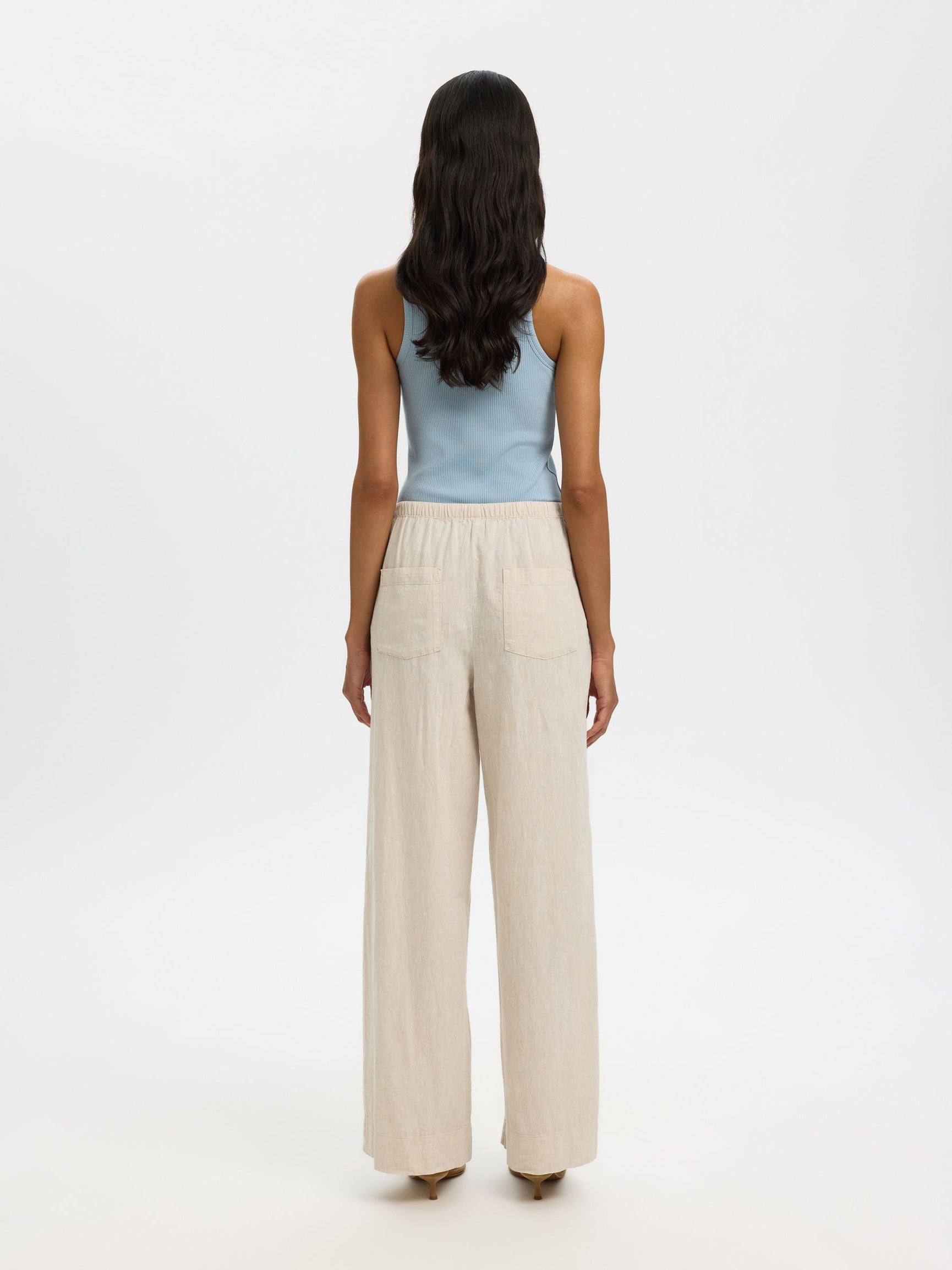 Woman wearing a light blue sleeveless top and beige high-waisted pants on a white background