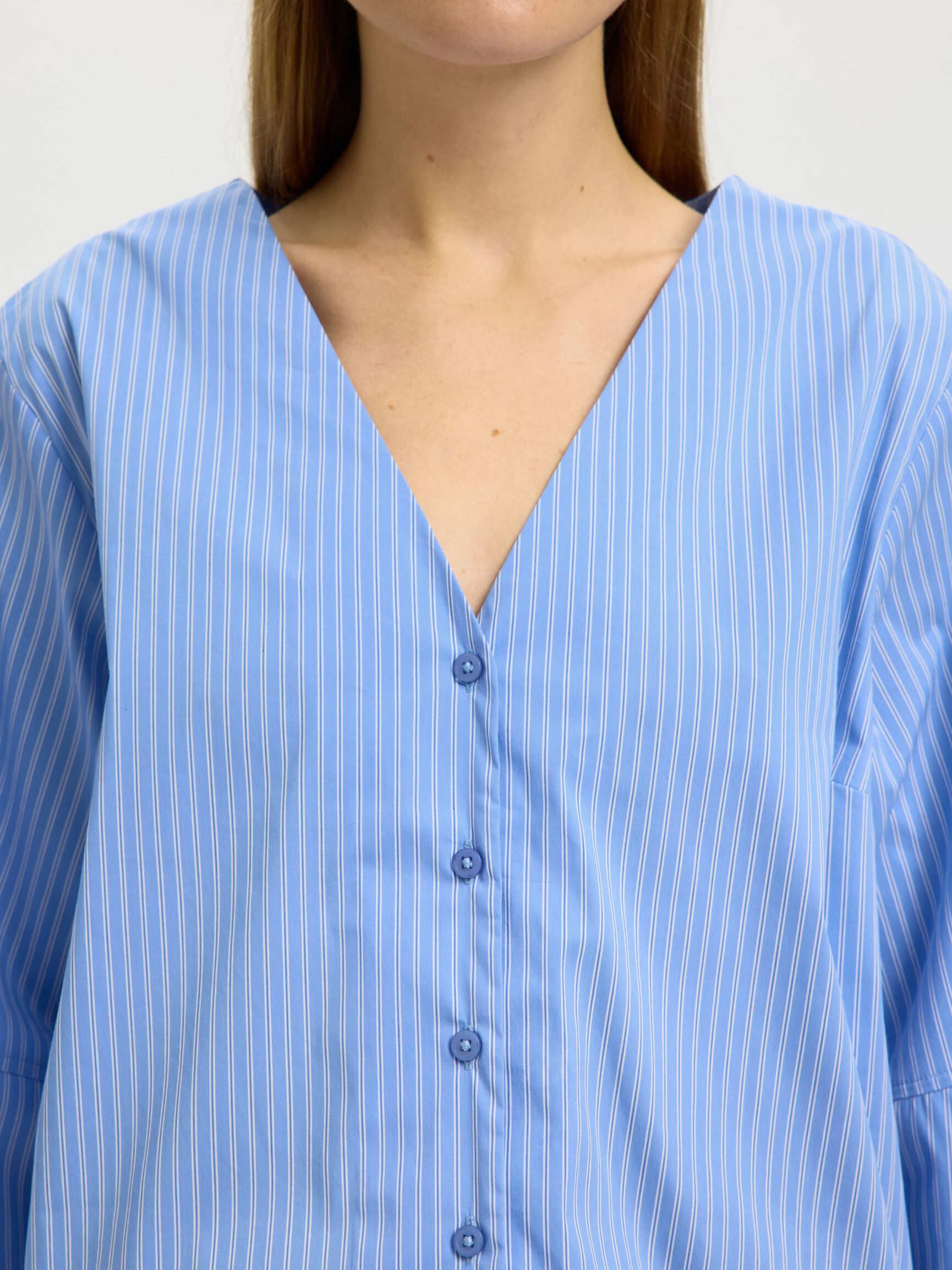 Close-up of a person wearing a blue striped shirt with a plain background