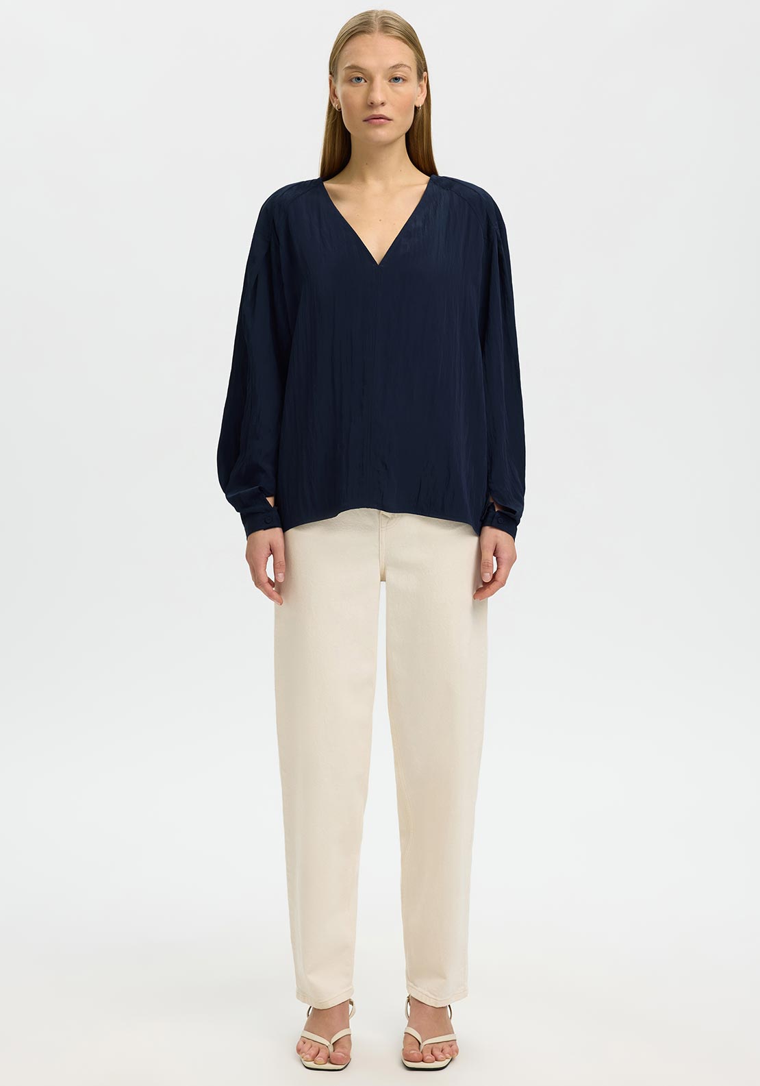 Woman wearing a navy blue top and beige pants on a white background