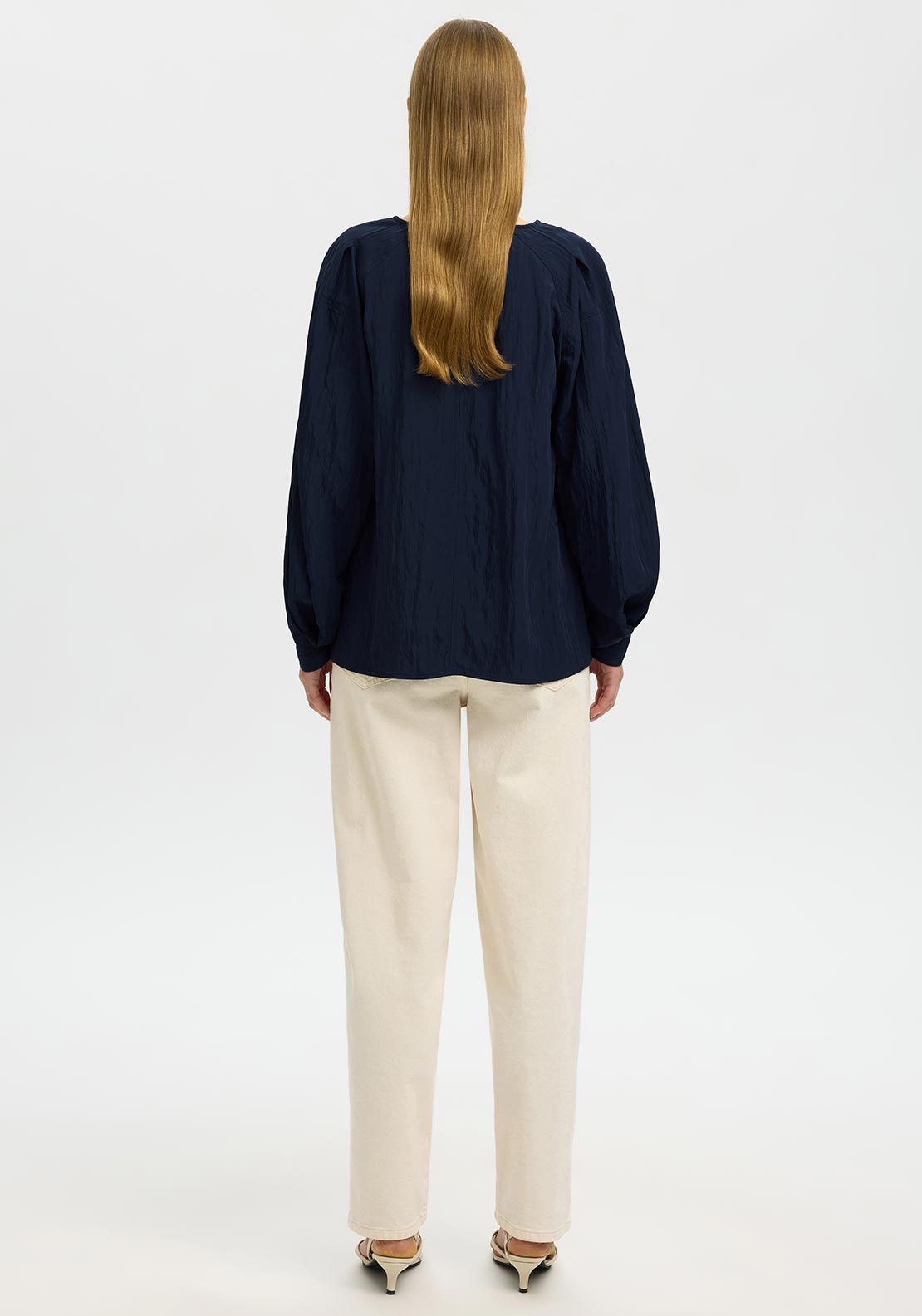 Person wearing a navy blue top and beige pants on a white background