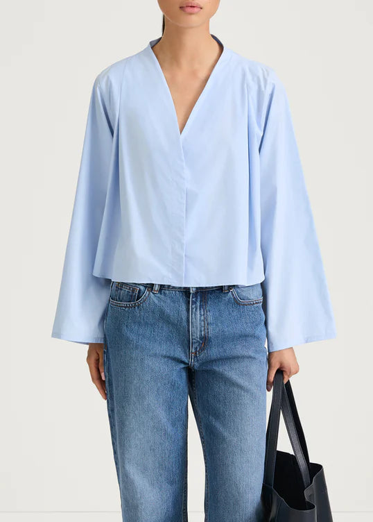 Person wearing a light blue blouse and jeans, holding a black tote bag on a white background