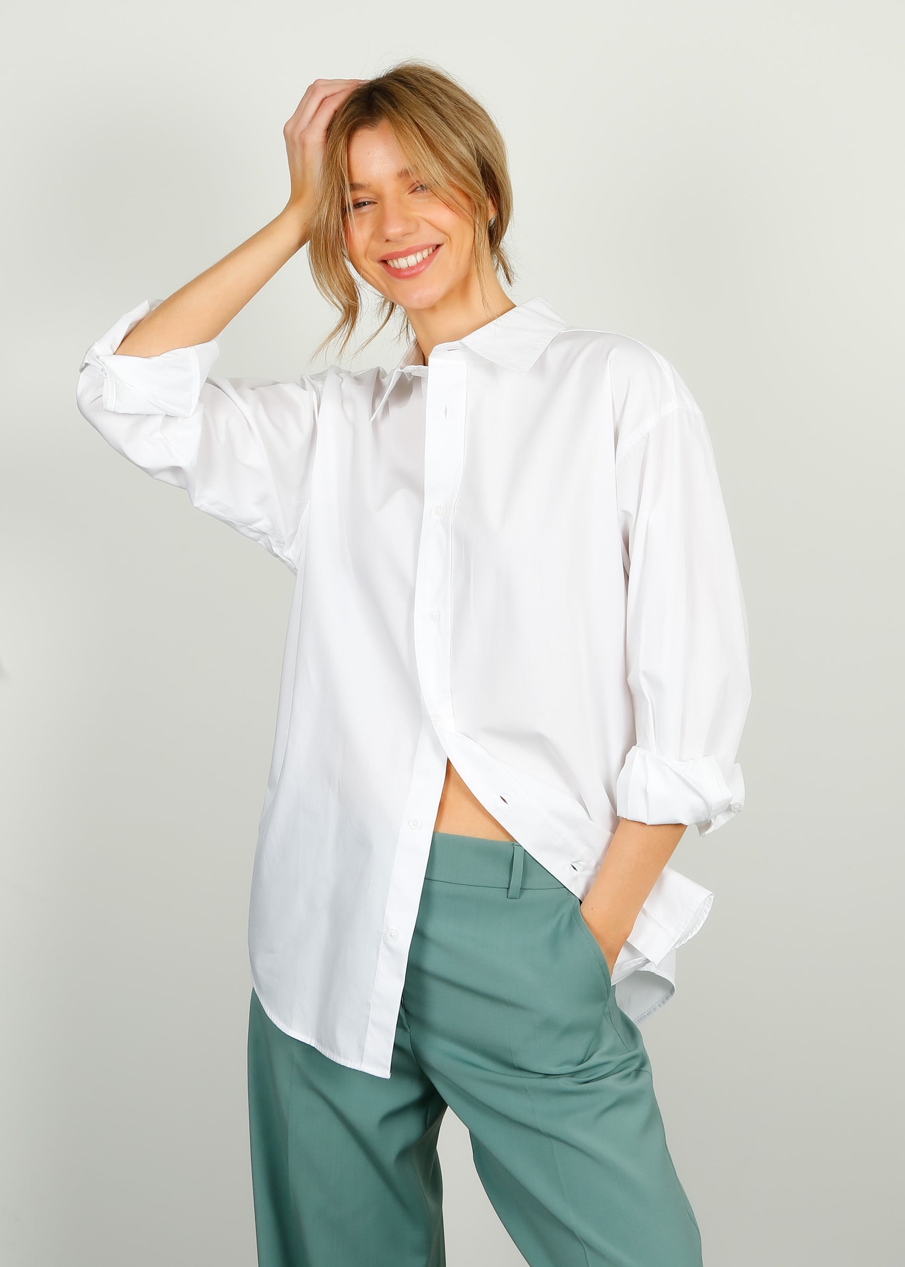A woman smiling, wearing a white cotton shirt with a classic collar and front button fastening, paired with green trousers.
